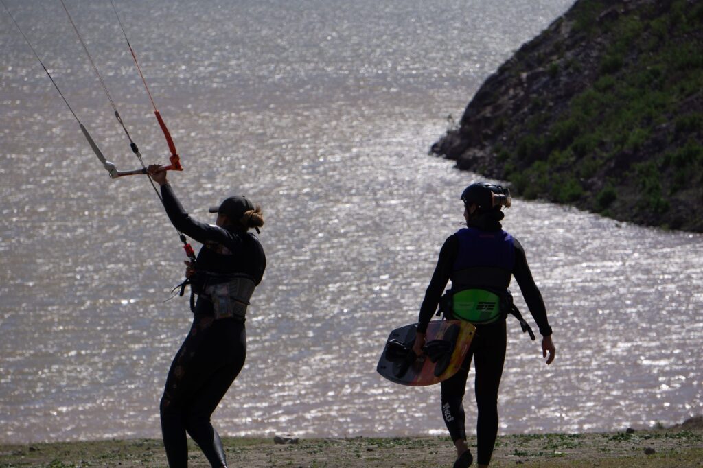 Dos kitesurfistas a contraluz en la orilla del Embalse Puclaro, uno con la barra del kite y otro con la tabla