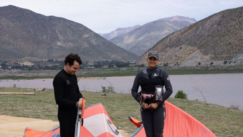 Dos riders sonriendo mientras preparan sus kites naranjos en la orilla del Embalse Puclaro, Valle de Elqui